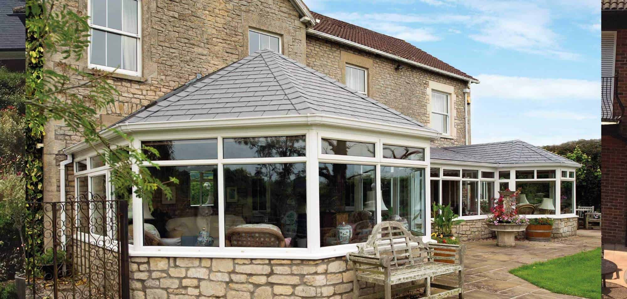 Guardian Warm Roof installation featuring a modern conservatory with a slate roof, surrounded by a stone exterior and garden elements, emphasizing quality craftsmanship and design.