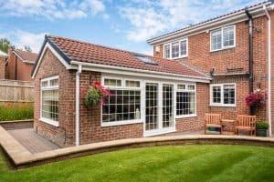 Tiled conservatory roof on a brick extension, featuring large windows, a landscaped garden, and seating area, illustrating modern conservatory design and benefits of solid roofing solutions.